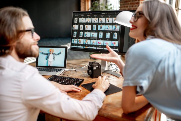 Young couple of photographers working with woman's portraits at the working place with two computers in the studio